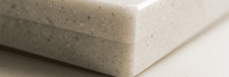 Macro photo of a Tristone worktop cross-section showing seamless construction, mineral flecks in a satin-matt resin, and a polished chamfered corner. The non-porous, velvety texture and engineered details highlight the material’s structure and understated luxury.