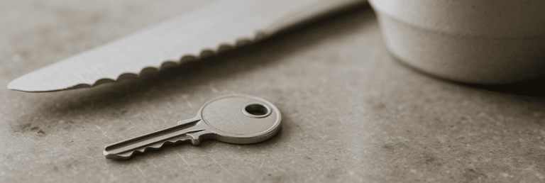 Macro photo of a Caesarstone quartz worktop surface with a key, serrated knife, and ceramic mug resting on it, showing faint micro-scratches, mineral flecks, and natural imperfections under daylight in a modern white kitchen setting.