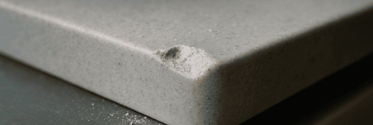 Macro photo showing a chipped edge on a Corian kitchen worktop with visible crumbs, dust, and utensils nearby. The image highlights the textured damage, subtle imperfections, and real-world causes of worktop chipping, ideal for explaining Corian surface vulnerabilities.